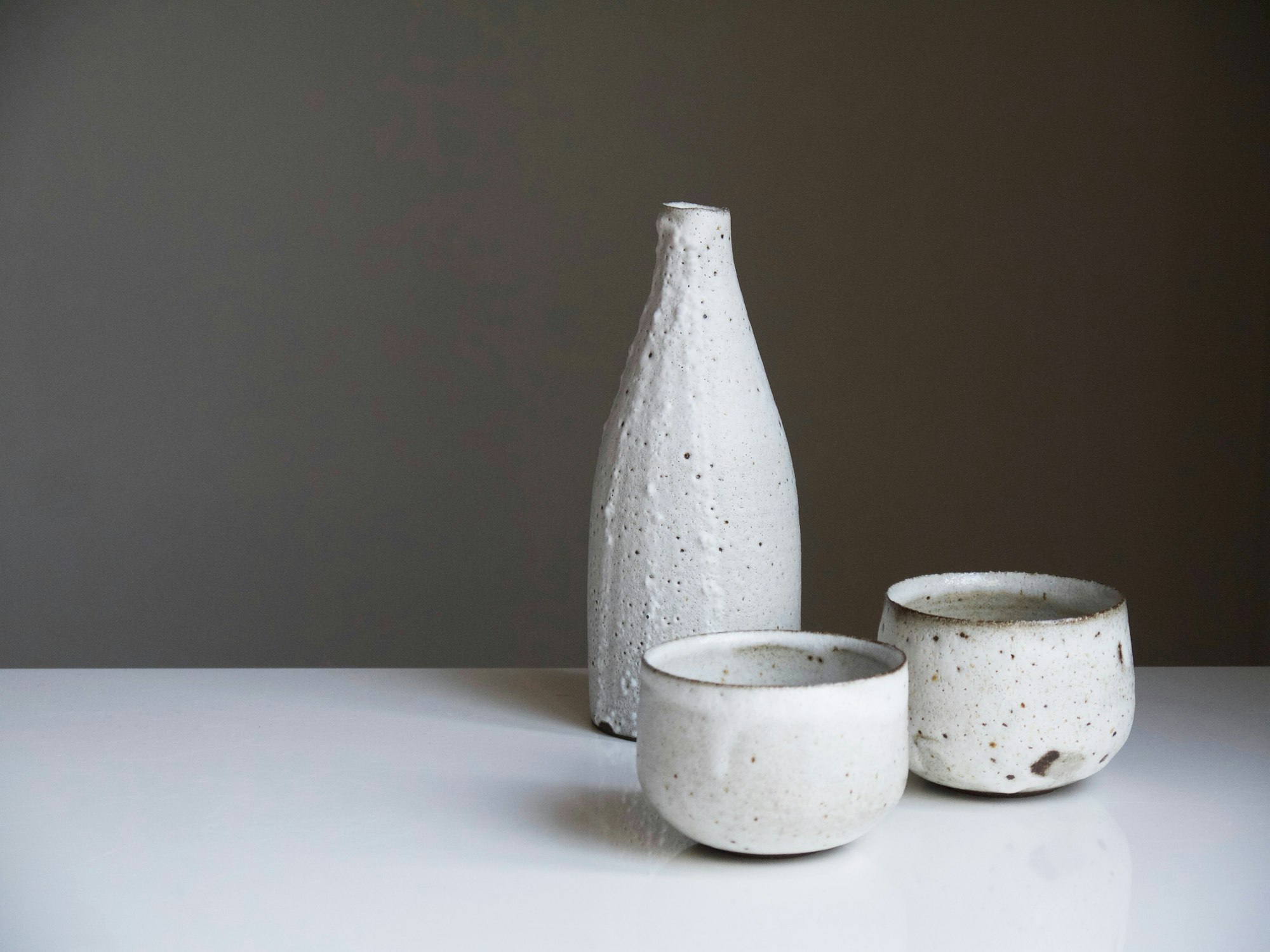 Biała ceramiczna butelka i dwie czarki na jasnym stole
